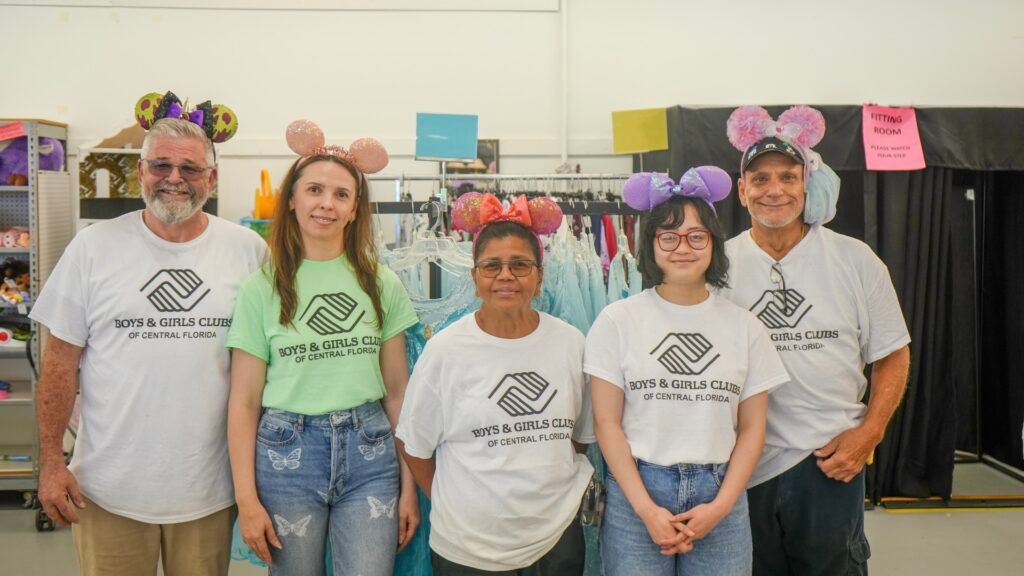 Five people wearing "Boys & Girls Clubs of Central Florida" shirts and decorative Mickey ears standing in front of clothing racks.