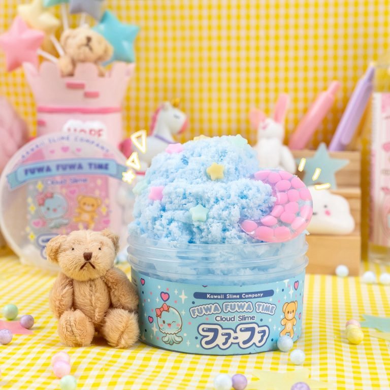 Blue cloud slime decorated with pastel stars and moons in a clear container, with a plush teddy bear beside it on a yellow gingham tablecloth.