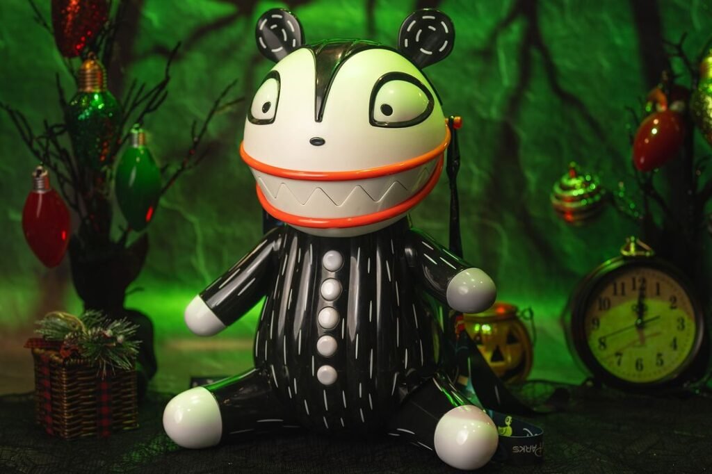 A large, black and white toy figure with a big, wide smile and buttoned black outfit, set in a spooky-themed environment with green lighting, decorative lights, a clock, and a festive basket in the background.