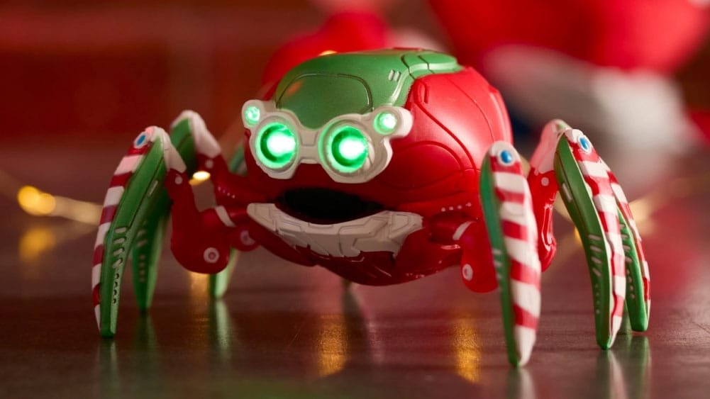 A colorful toy spider with a red and green body, glowing green eyes, and striped candy cane-like legs, set against a blurred festive background.
