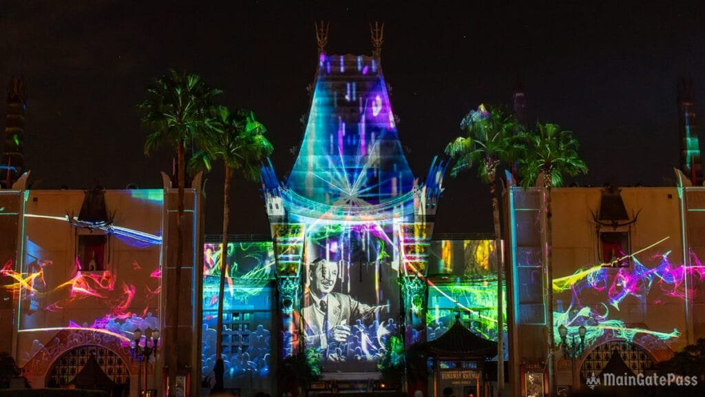 Vibrant light projections illuminating the facade of a building at night, featuring colorful patterns and an image of a man, framed by palm trees and a dark sky.
