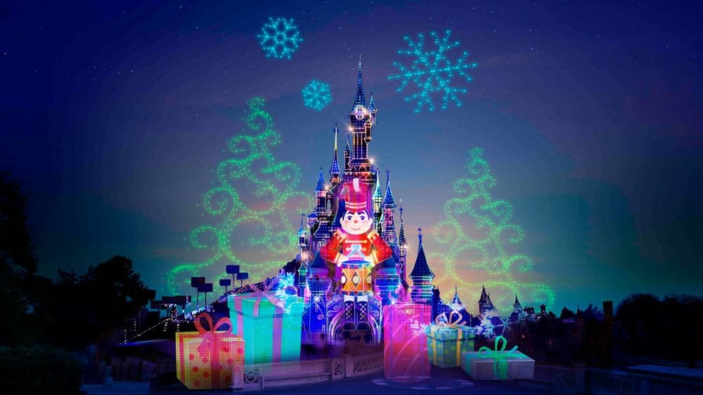 A brightly lit castle decorated for the holidays, featuring colorful projections of gifts, snowflakes, and a toy soldier against a nighttime sky.