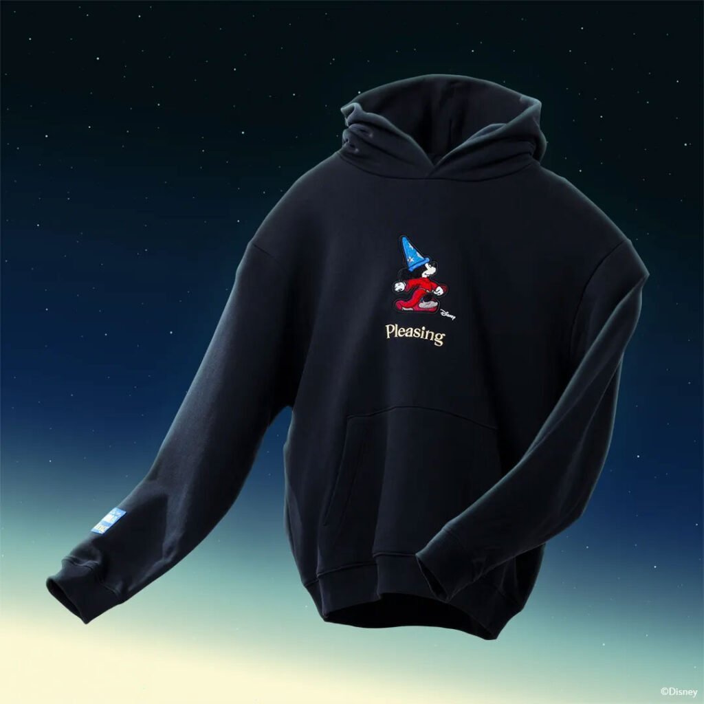 Black hoodie featuring an embroidered design of a character in a blue hat, with the word "Pleasing" below it, set against a starry background.