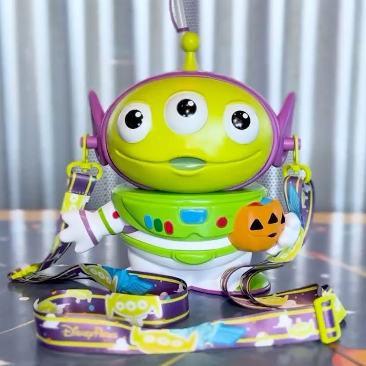 Toy alien holding a small pumpkin bucket with a colorful lanyard attached.