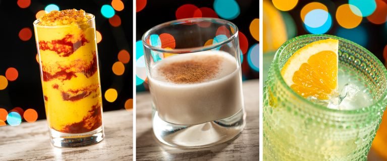 Three vibrant drinks displayed: a tall glass with a layered yellow and red beverage, a short glass filled with a creamy light-colored drink topped with a sprinkle of brown, and a textured green glass containing a clear drink with a slice of orange. The background features colorful bokeh lights.