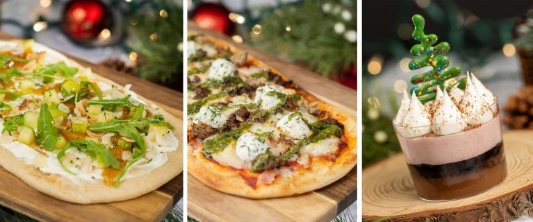 Three dishes on wooden serving boards: the left features a flatbread topped with vegetables and sauce, the center showcases a pizza with various toppings and dollops of cream, and the right displays a dessert in a glass with layers of chocolate and cream, topped with a green chocolate decoration resembling a Christmas tree.