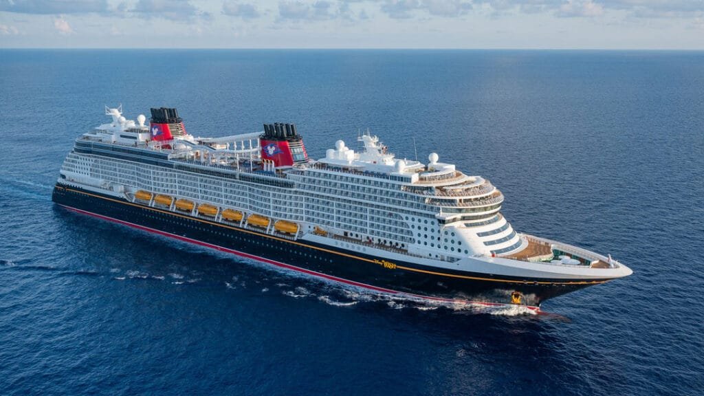 A large cruise ship sailing on the ocean with multiple decks, featuring red and black exteriors and yellow lifeboats.