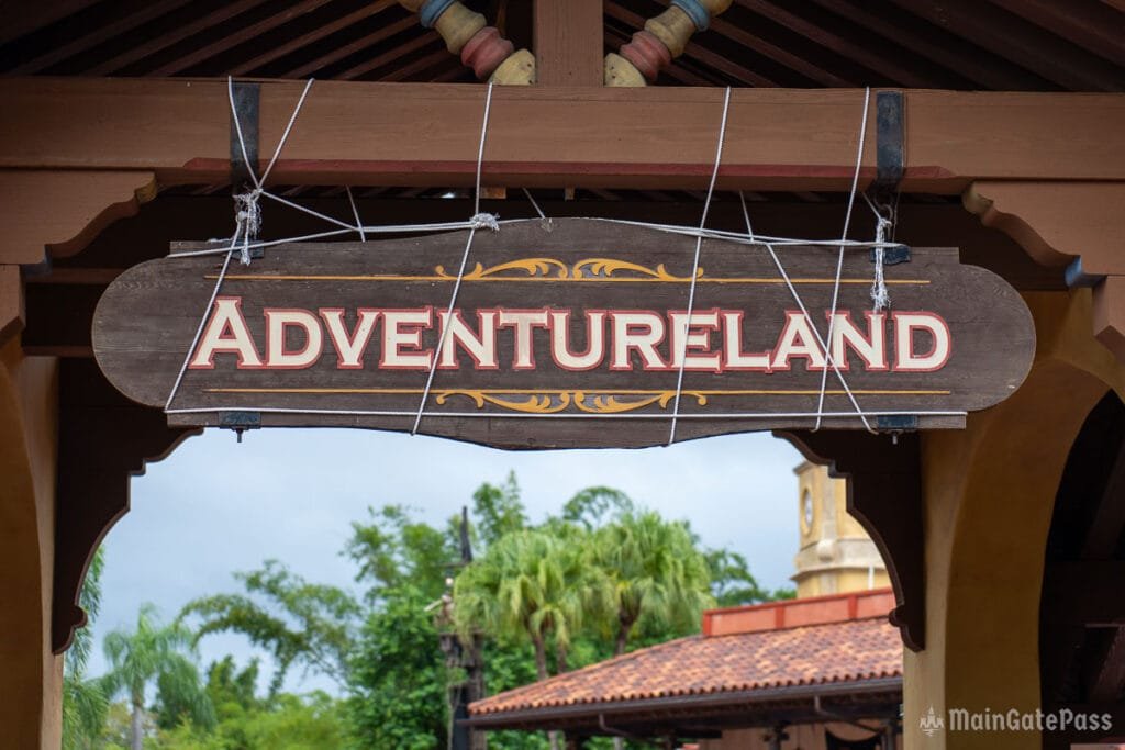 Sign for "Adventureland" hanging from a building with tropical foliage in the background.
