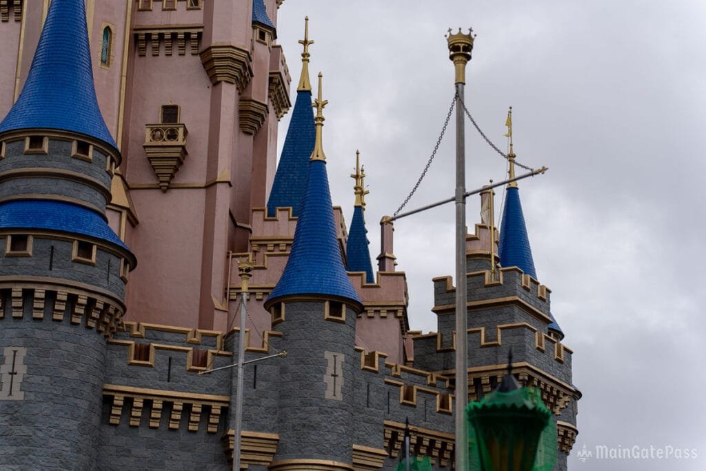 A close-up view of a castle featuring blue spires, gray stone walls, and gold accents, under a cloudy sky.