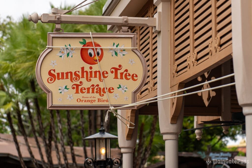 Sign for "Sunshine Tree Terrace" featuring an orange character, with greenery in the background.