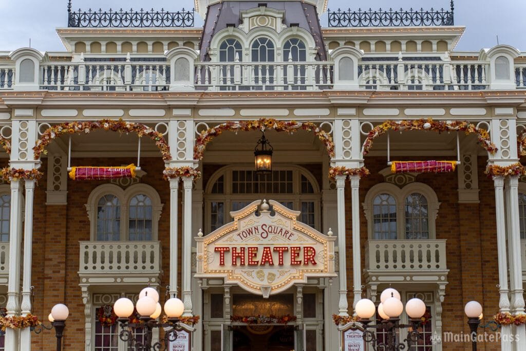 Front view of the Town Square Theater, featuring a decorative sign that reads "THEATER" in bright red letters, surrounded by autumn-themed decorations, with a series of large white lanterns in the foreground and architectural details in a Victorian style.