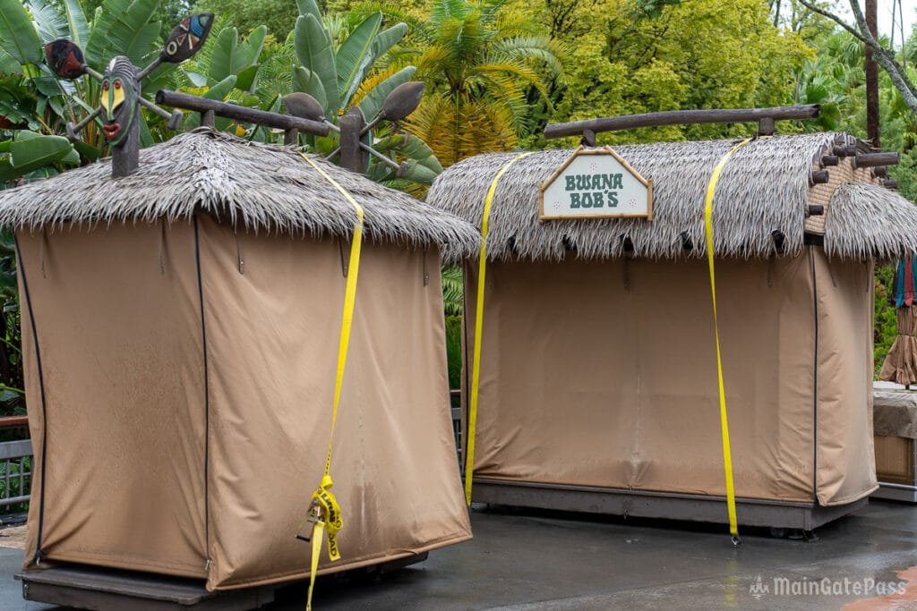 Two thatched-roof huts, one marked "Bwana Bob's," are secured with yellow straps, surrounded by lush greenery.