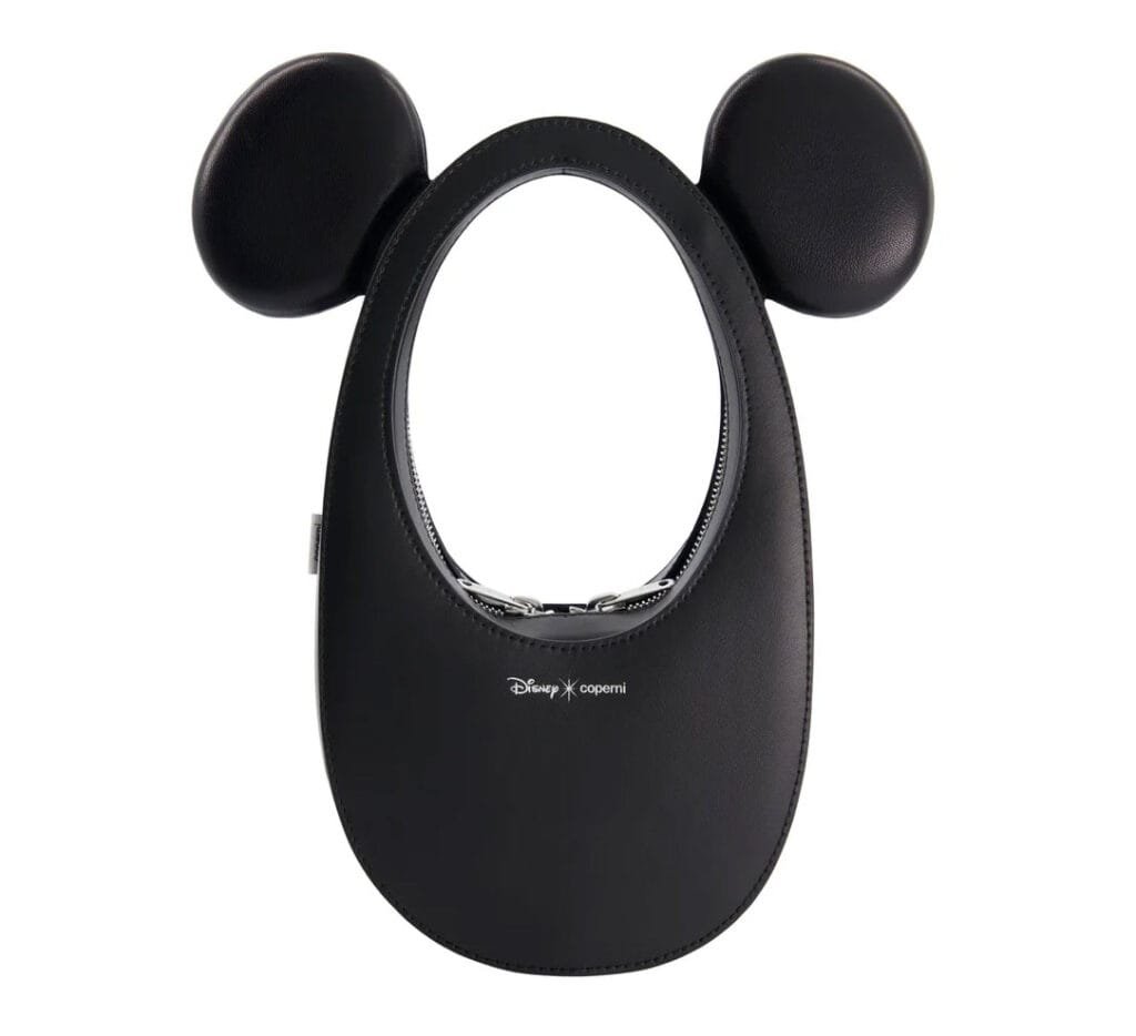 A black leather bag with a rounded shape and two circular ears on the top, designed in collaboration with Disney and Coperni, featuring a zipper closure and a logo at the front.
