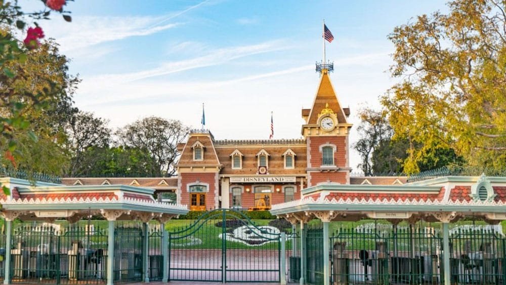 A view of the Disneyland entrance, featuring the iconic ticket booth, a clock tower, and lush greenery.