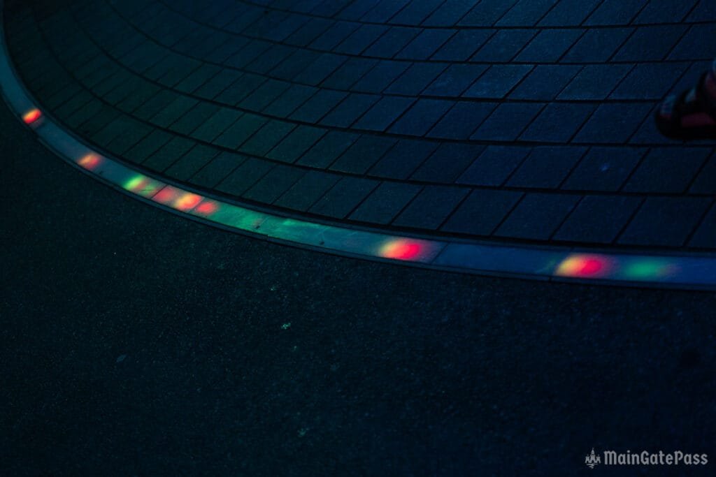 A curved pavement edge with colorful light reflections, set in a dimly lit environment.