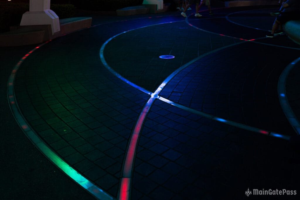 A dark pathway with colorful LED lights embedded in the ground, creating a winding, illuminated design.