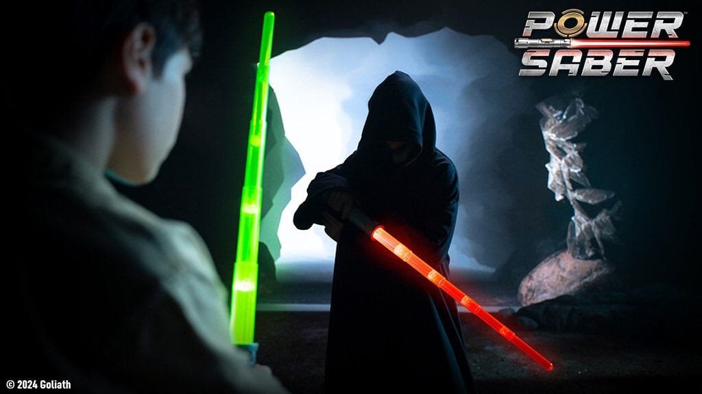A child in a light-colored shirt holds a green toy lightsaber, facing a cloaked figure wielding a red toy lightsaber in a dark cave-like setting. The scene is illuminated by the lightsabers' glow.