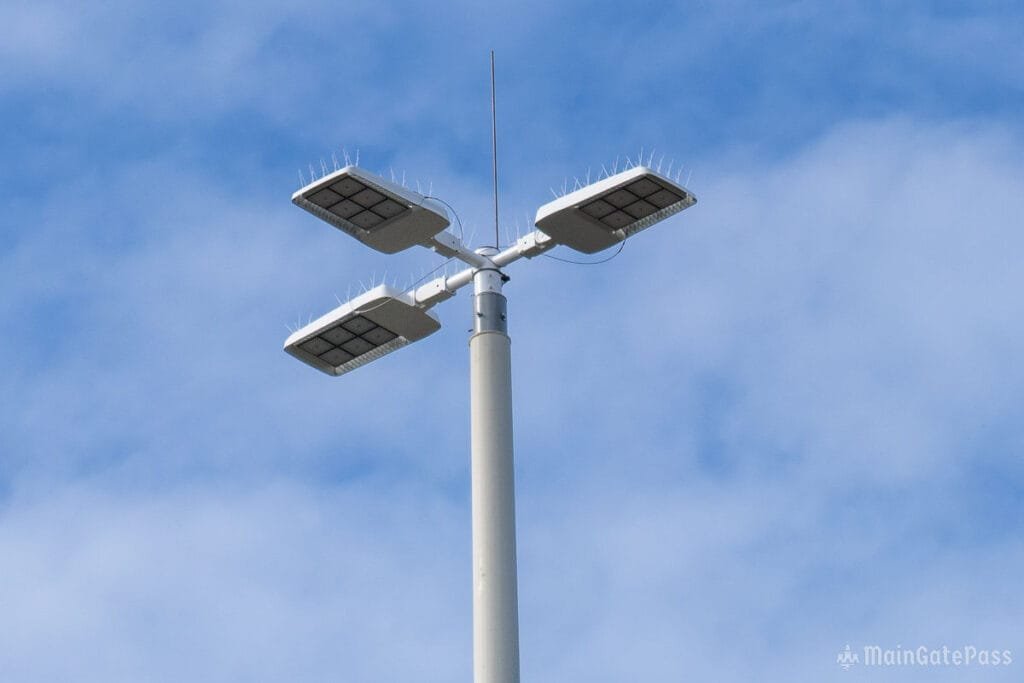A tall solar streetlight with four solar panels mounted on top, set against a blue sky with scattered clouds.