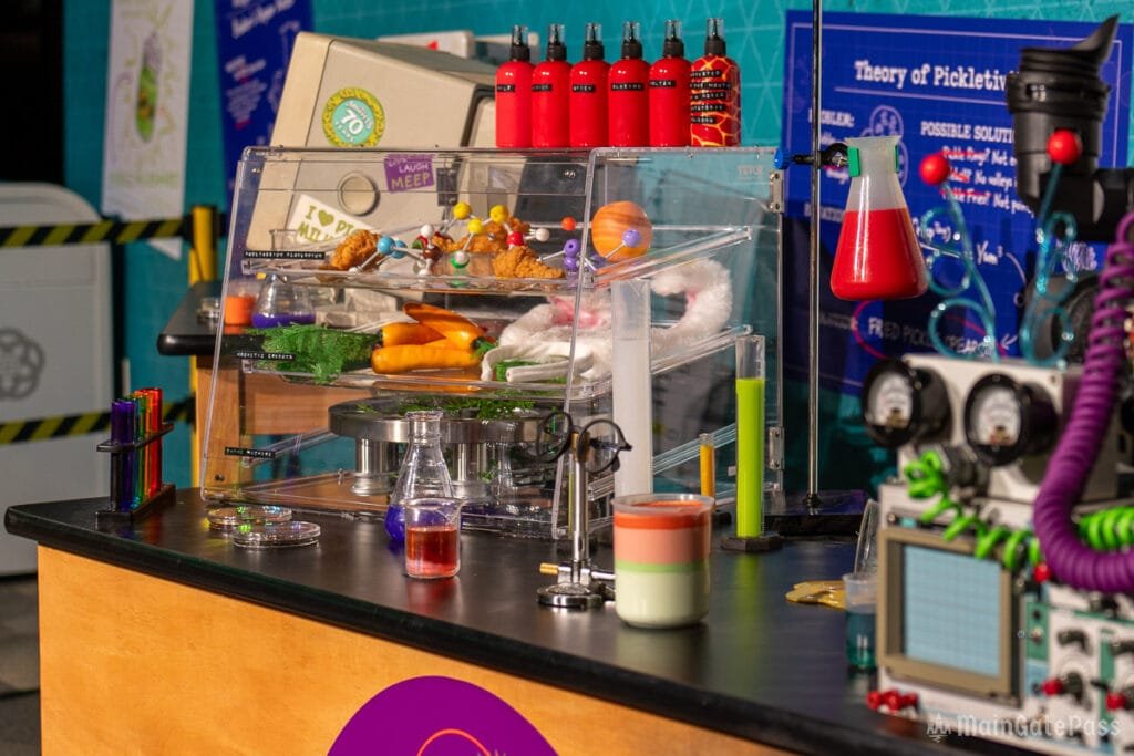 A colorful science-themed display featuring various laboratory equipment, containers with colored liquids, food items, and playful decorations, all set on a black tabletop.