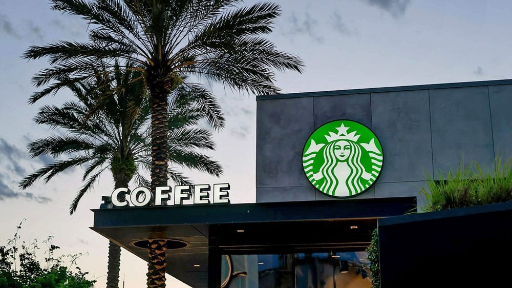 A Starbucks coffee shop entrance with palm trees, featuring a green circular logo and signage that reads "COFFEE."