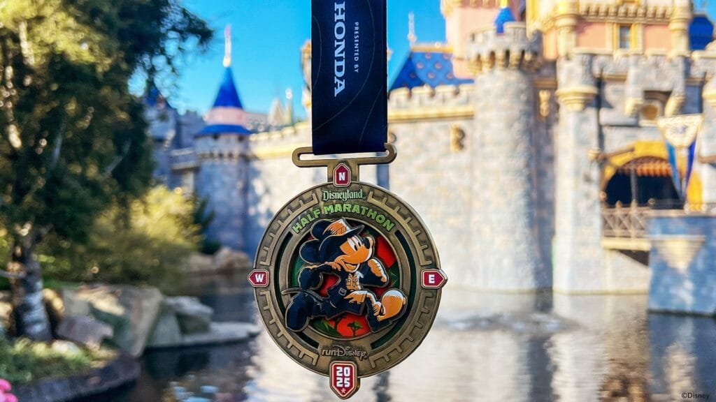 A medal for the Disneyland Half Marathon featuring a cartoon character running, with a castle in the background and a blue sky.