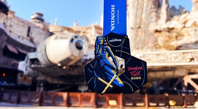 A medal with a black and blue design featuring a character holding a lightsaber, with "Disneyland 10K 2025" written on it, is hanging in front of the Millennium Falcon in a themed area.