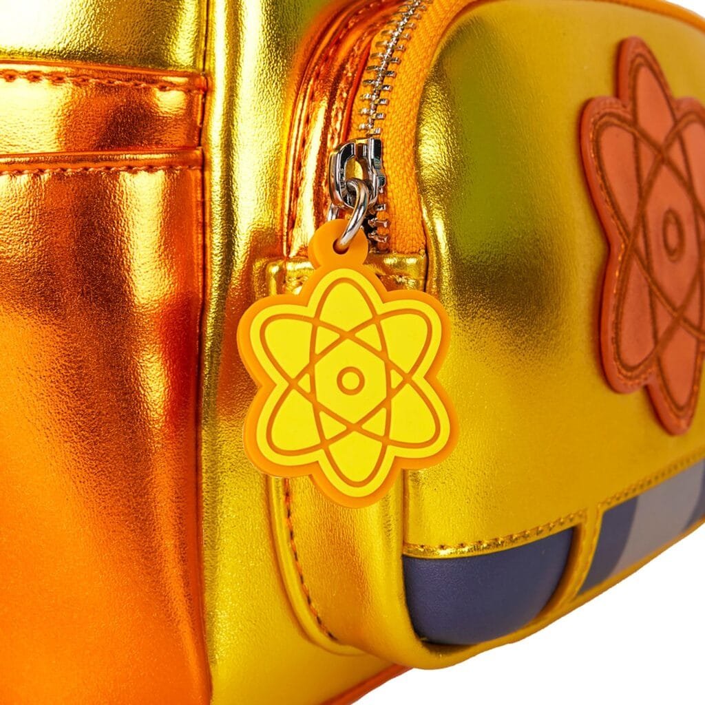 Close-up of a shiny, metallic yellow and orange bag featuring a zipper, an orange flower-shaped patch, and a yellow atomic symbol keychain attached to the zipper.