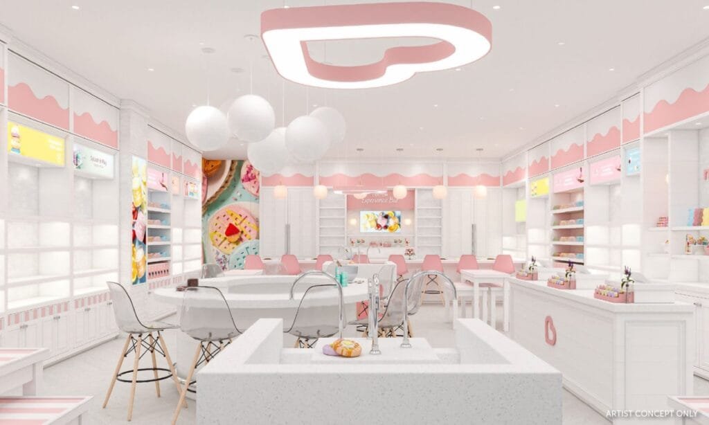 A brightly decorated, modern ice cream shop interior featuring pink and white color scheme, clear stools, round white pendant lights, and a display area with colorful desserts. The back wall showcases an 'Experience Bar' sign with a colorful dessert image.
