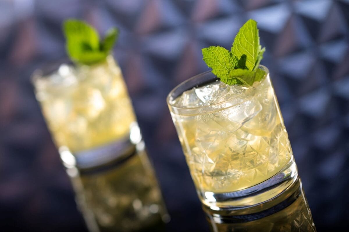 Two glasses of cocktails with ice and mint garnish on a reflective surface.