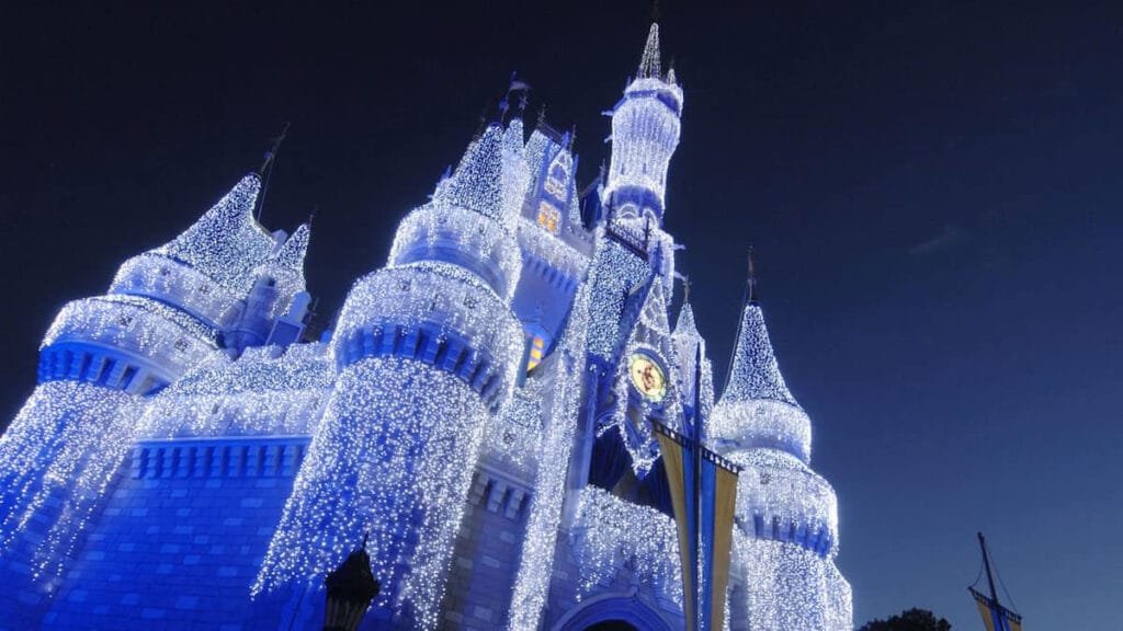 A grand castle adorned with shimmering blue and white lights, set against a night sky, showcasing its towers and intricate architectural details.