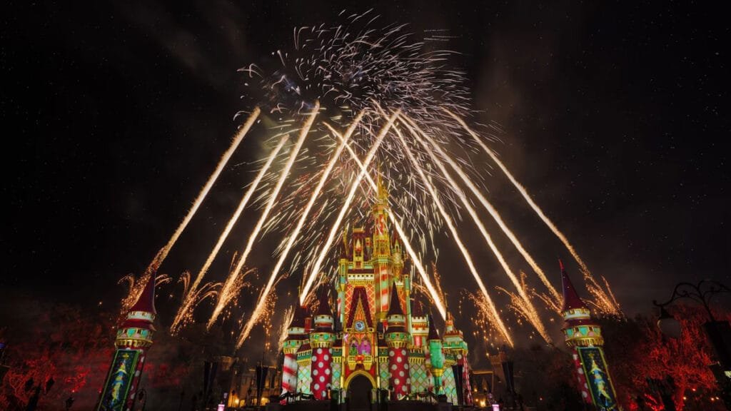 A vibrant castle illuminated with colorful projections at night, surrounded by colorful fireworks shooting into the sky against a dark backdrop.